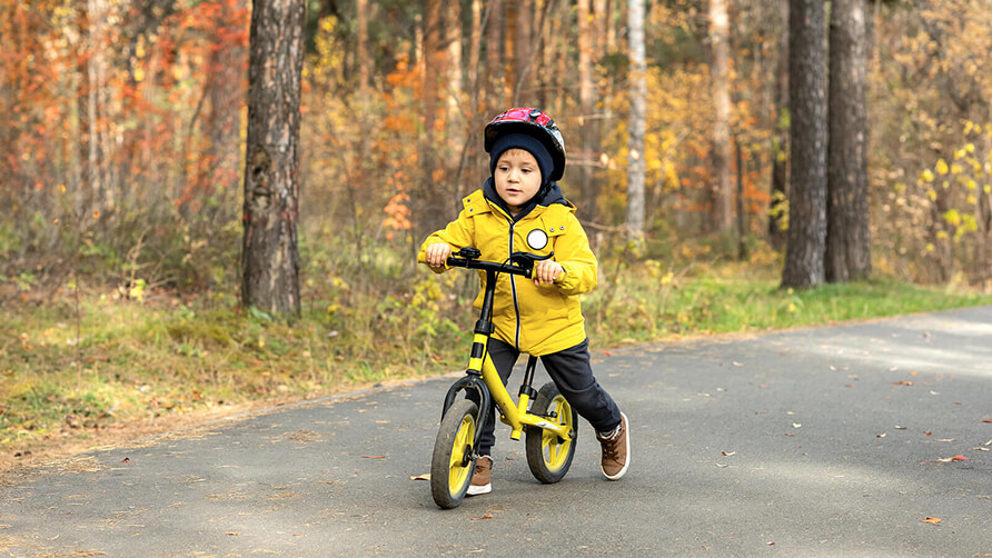 Kleine jongen op een geel loopfietsje in het bos